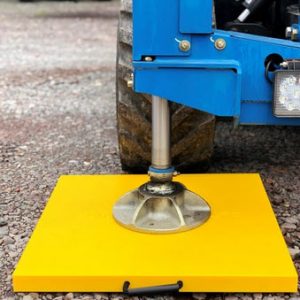 Crane outrigger foot on bright yellow square pad on gravel ground